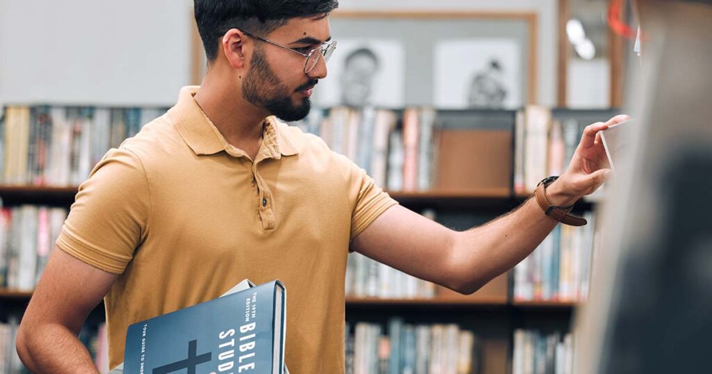 A man with beard and glasses at the library looking for books to answer his questions about being a Christian