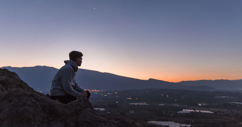 Young man on a hillside at sunset considering becoming a Christian