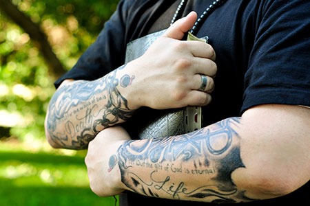 A man hugging his Bible with tattoos on both of his arms