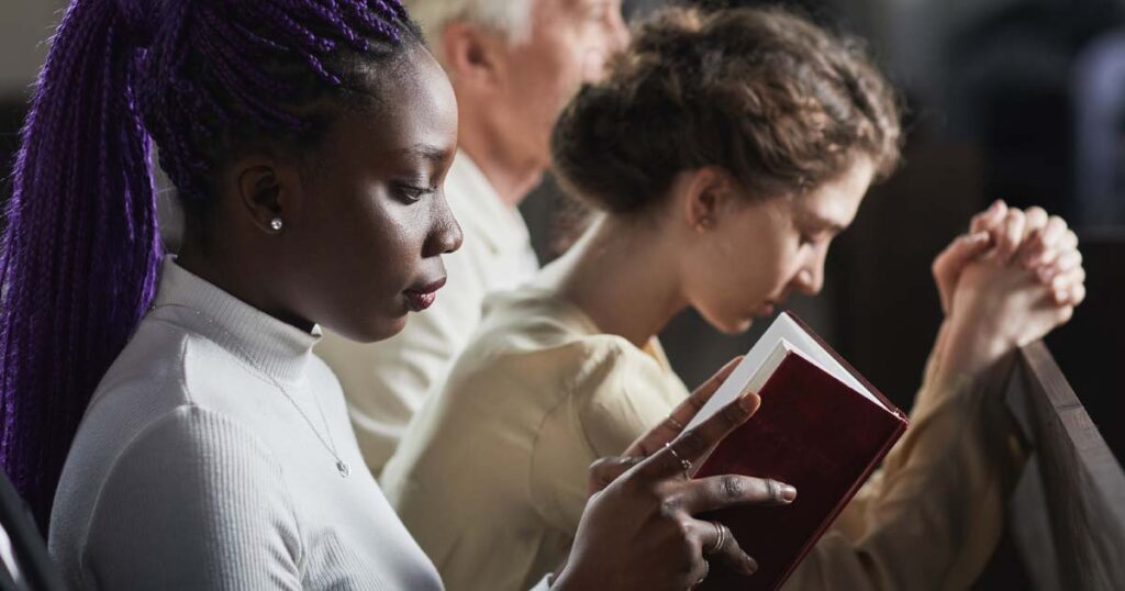 Several people sitting in a pew at church praying and reading the Bible