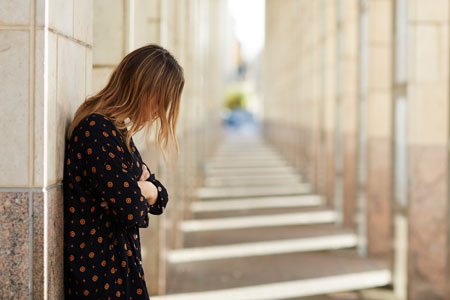 Woman standing in between columns of a building with her head down