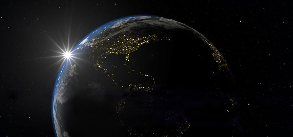 The western hemisphere of earth seen from space at night with the sun setting on the far side