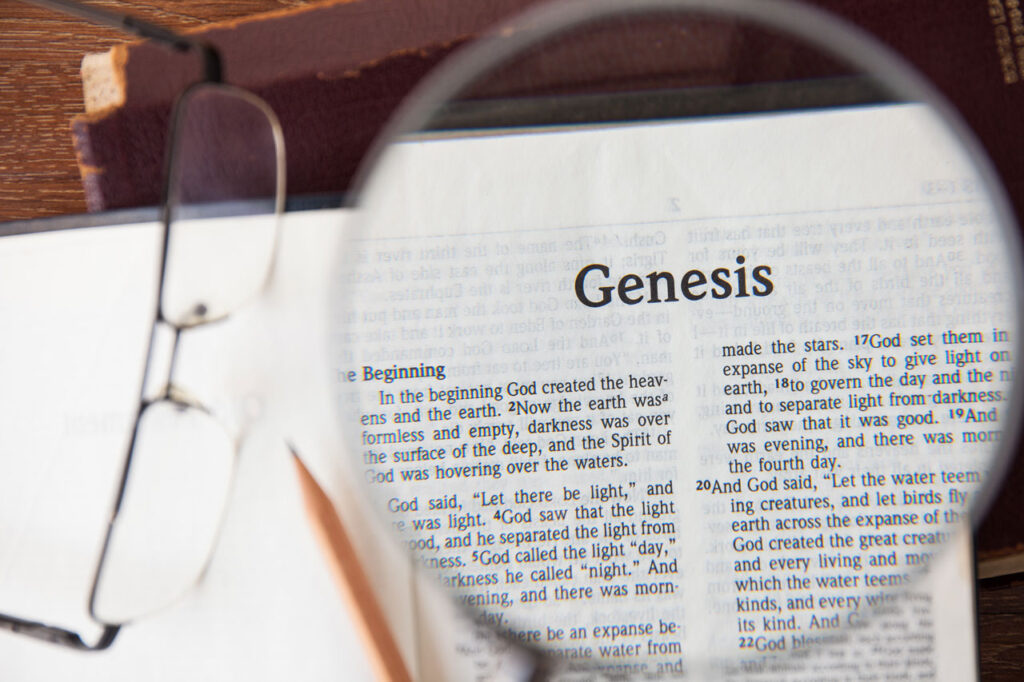 A magnifying glass zooming in on the first page of the Book of Genesis in the Bible