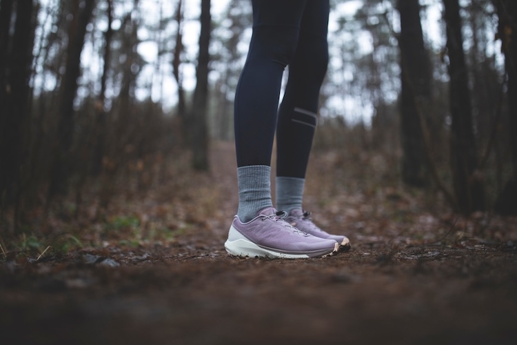 Person wearing running shoes standing on a dirt path in a forest.