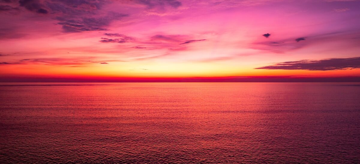 A panoramic view of a serene ocean at sunset, featuring vibrant shades of purple, pink, and orange in the sky, representing the second day of creation.