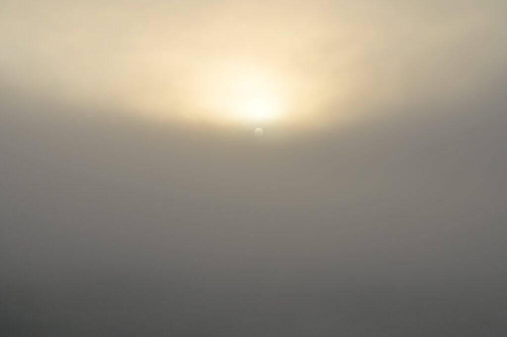 A hazy sky with a faint sun barely visible through the fog, representing the fourth day of creation.