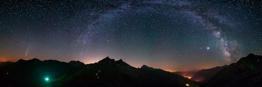 A panoramic view of a star-filled night sky with the Milky Way arching above dark mountain peaks, representing the first day of creation.