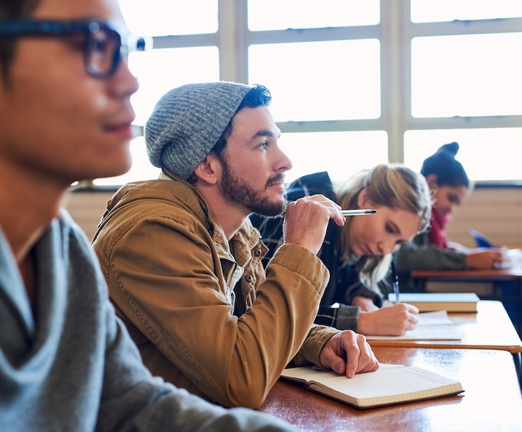 Students sitting at classroom desks engage in thoughtful study, representing classroom discussions about evolution.