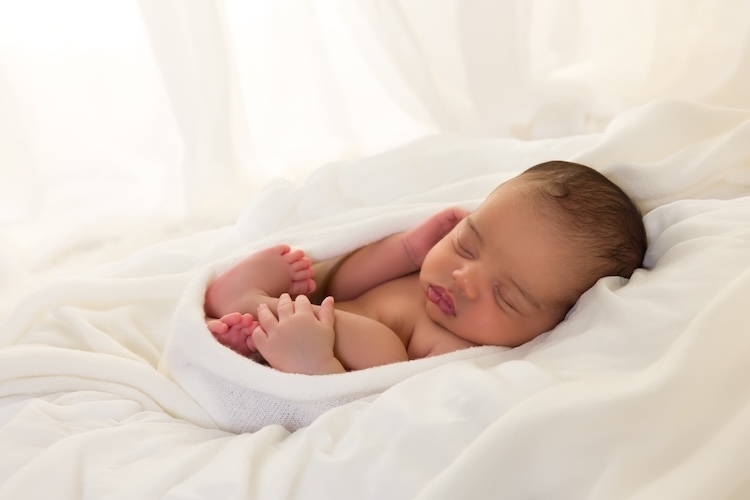 A newborn wrapped in a soft white blanket and resting on a bed of layered white fabric, used to illustrate infancy and early human life within broader discussions about what the Bible says about abortion.
