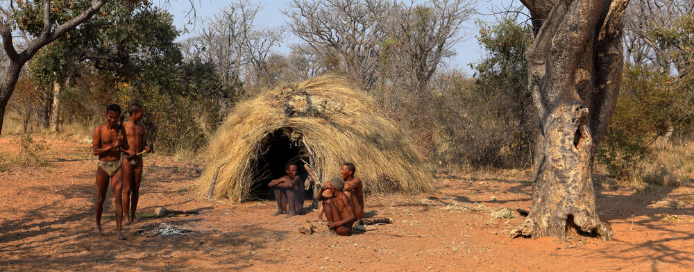 Traditional hunter-gatherer community near a grass dwelling, representing early human environments related to what Adam and Eve may have looked like.
