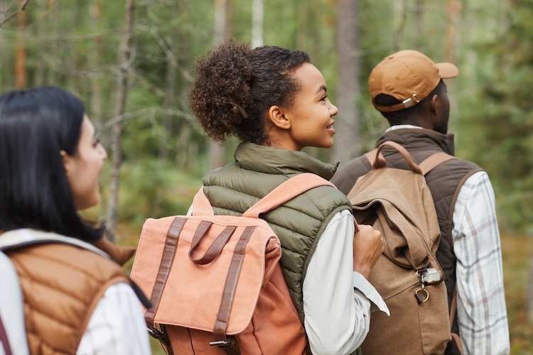 Diverse group of hikers with backpacks walking through a forest trail, symbolizing modern human movement and migration.