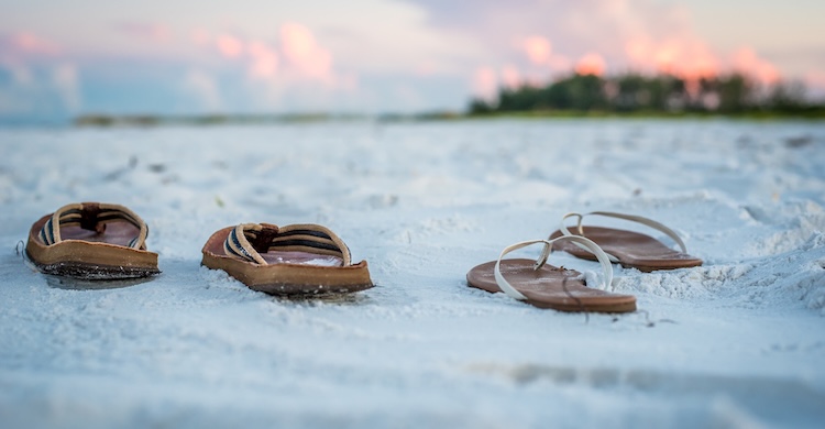 Two pairs of sandals lie on a serene, sandy beach at sunset.