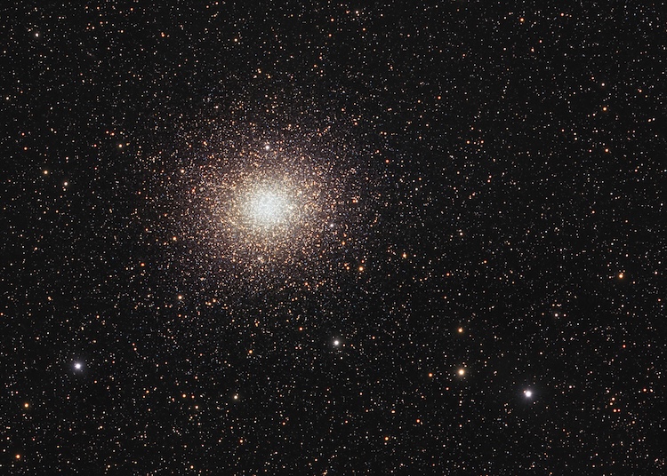 Dense star cluster with a bright, glowing center against a dark sky, surrounded by numerous stars.