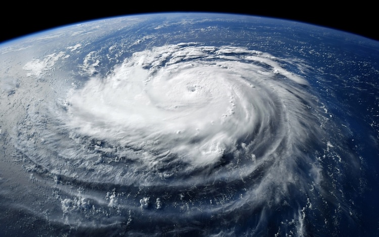 Satellite image of a large, swirling hurricane over a deep blue ocean. Thick clouds form a distinct spiral.