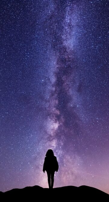 Silhouette of a person standing against a starry night sky, with the Milky Way galaxy vividly stretching above.