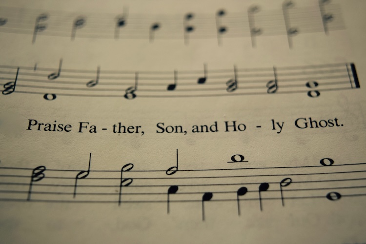 Sheet music displaying the line "Praise Father, Son, and Holy Ghost." Musical notes and staves are visible above and below the text.