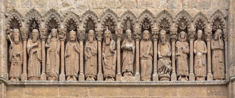 Stone carvings of Old Testament prophets standing in a row within arched niches on a Gothic cathedral façade.
