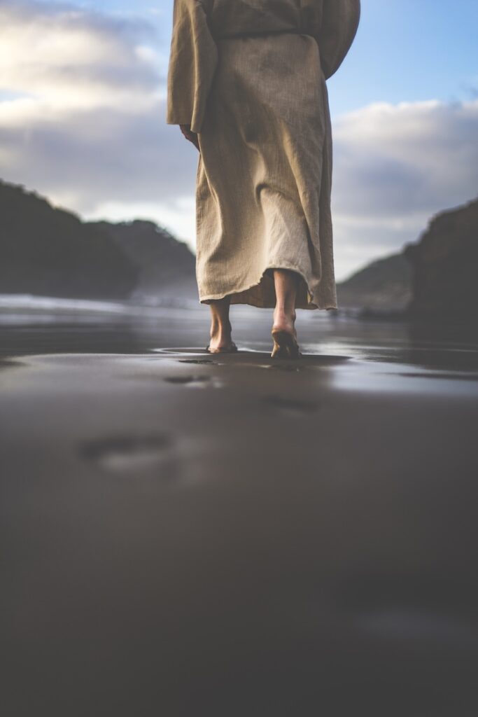 Jesus walking away along a shoreline, leaving footprints in wet sand, symbolizing the historicity of Jesus.