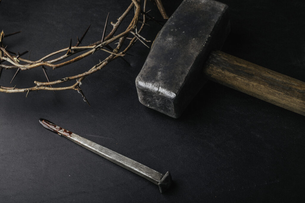 A crown of thorns, a hammer, and a blood-stained nail arranged together, symbolizing Jesus’ crucifixion and the instruments of his suffering.