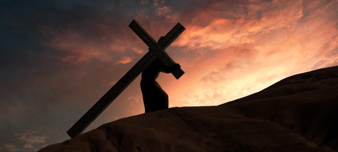 Silhouette of Jesus carrying the cross along a hill at sunset, the glowing sky framing the scene and reflecting the sorrow of the crucifixion of Christ.