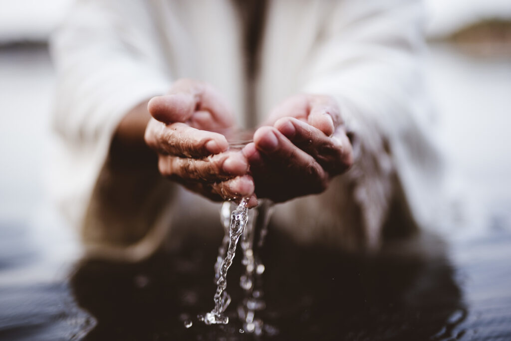 Hands gently scooping water, symbolizing cleansing and renewal, illustrating how Jesus’ death is an invitation for us to receive grace and new life.