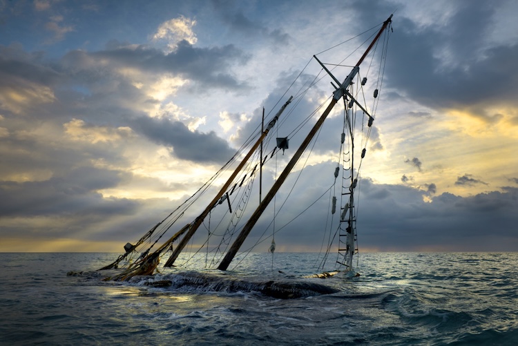 A shipwreck partially submerged in the ocean with a dramatic sky filled with clouds during sunset.