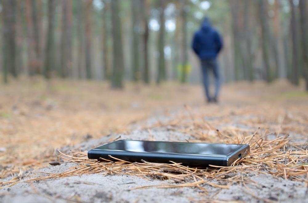 Smartphone left on the forest floor while a person walks away in the background, symbolizing breaking free from social media addiction.