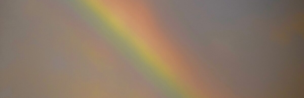 Softly blurred rainbow against a muted gray sky.