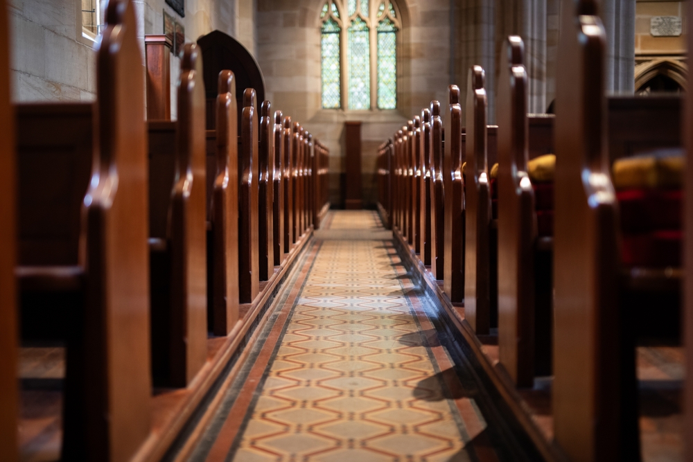 Interior aisle of a traditional church with wooden pews and stained glass windows, reflecting the history of Christianity.