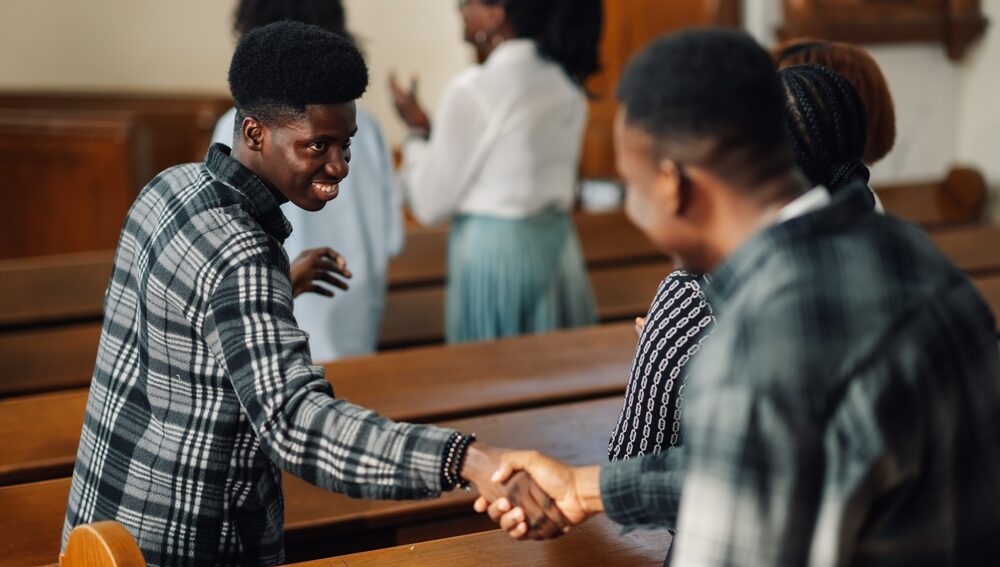 Two men shaking hands inside a church sanctuary, illustrating what the church is—a community of believers gathering in fellowship and worship.