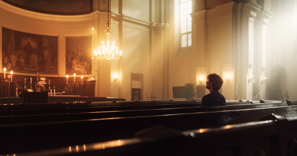 A person sitting alone in a dimly lit church, contemplating whether all religions lead to God.