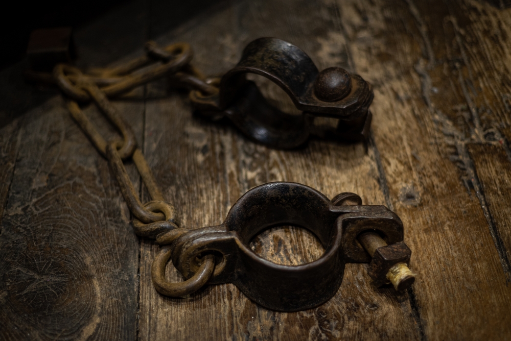 Metal shackles resting on a wooden surface, symbolizing biblical slavery and the treatment of human beings as property.