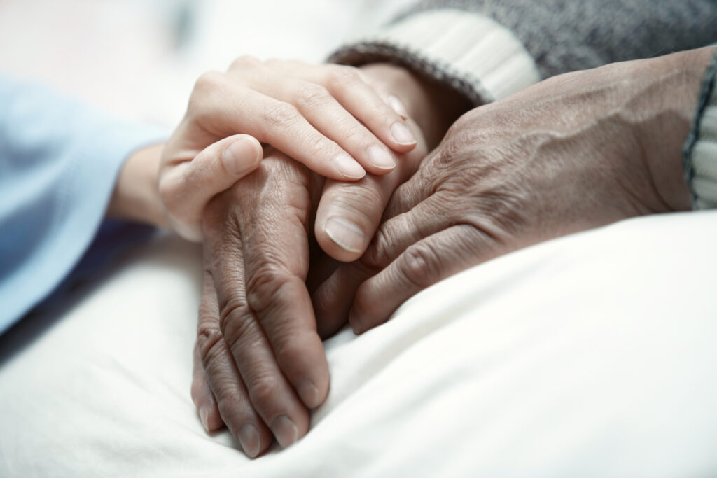 Person holding an elderly patient’s hand in comfort while reflecting on hope and questions about life after death.