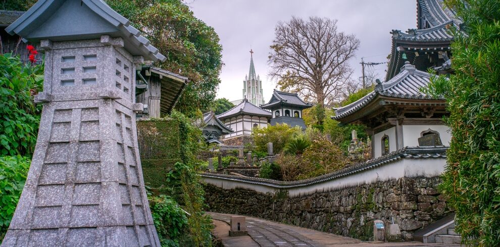 Pathway leads through a serene garden with traditional Japanese architecture, stone lanterns, and lush greenery.