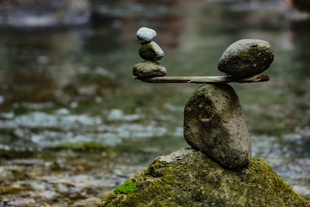 A balanced stack of stones on a mossy rock in front of a blurry stream.