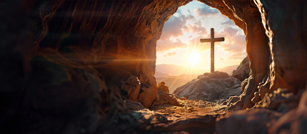 A crucifixion cross viewed from an empty tomb with the sun rising in the background, evoking hope.