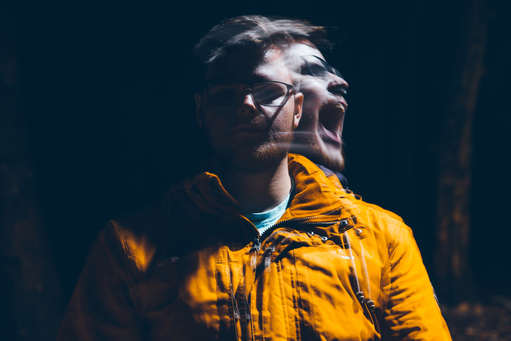 Man in orange jacket facing the viewer with a motion-blur of his head turned and yelling as if demon possessed or during an exorcism.