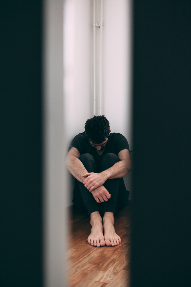 Man in a black shirt sitting with his arms crossed and head down surrounded by shadows.