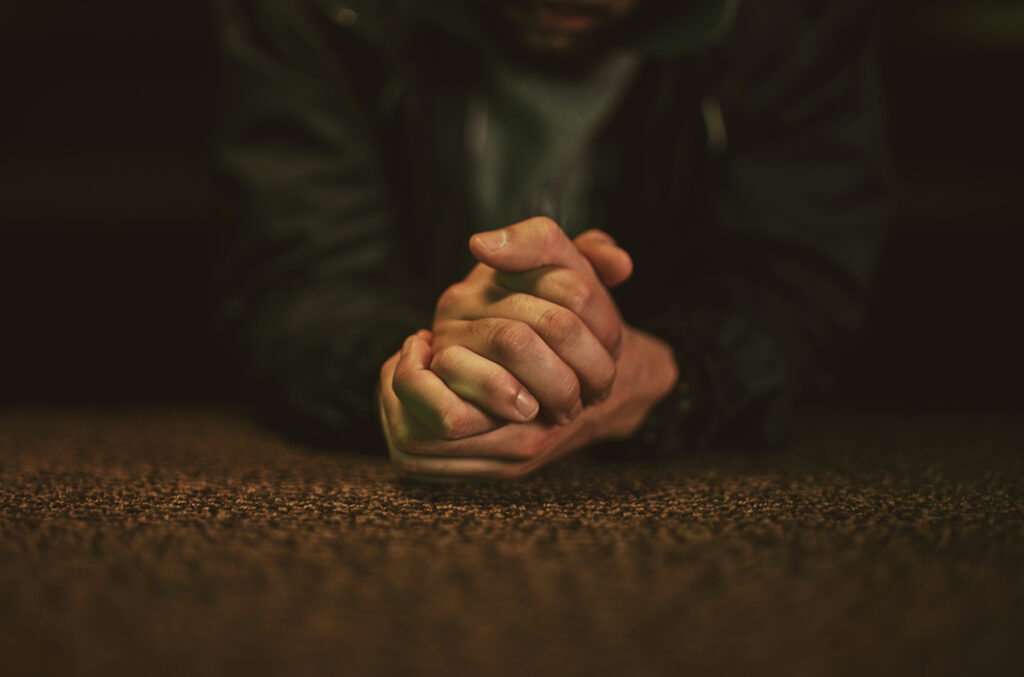 Man with clasped hands in prayer, reflecting on the question “is God real.”