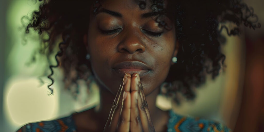 A woman with eyes closed and hands held together in prayer with soft light and warm colors surrounding the scene, symbolizing the importance of prayer and other spiritual disciplines in spiritual warfare.