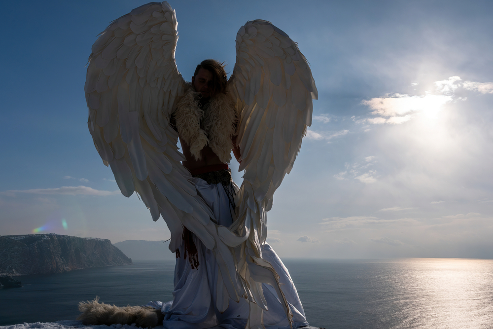 Graphical image of an angel with white wings on a cliff overlooking the ocean