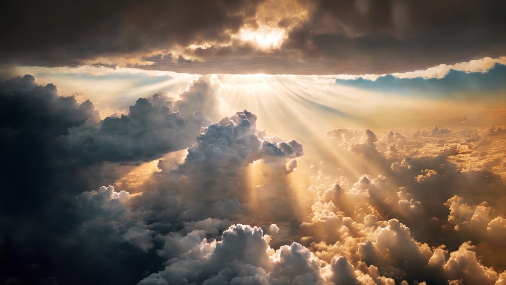 Light rays filter through dark, fluffy clouds against a dramatic sky.