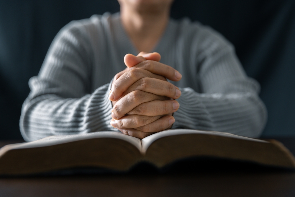 Hands clasped in prayer over an open Bible, symbolizing reliance on prayer and Scripture in spiritual warfare and the ongoing battle within the spiritual realm.