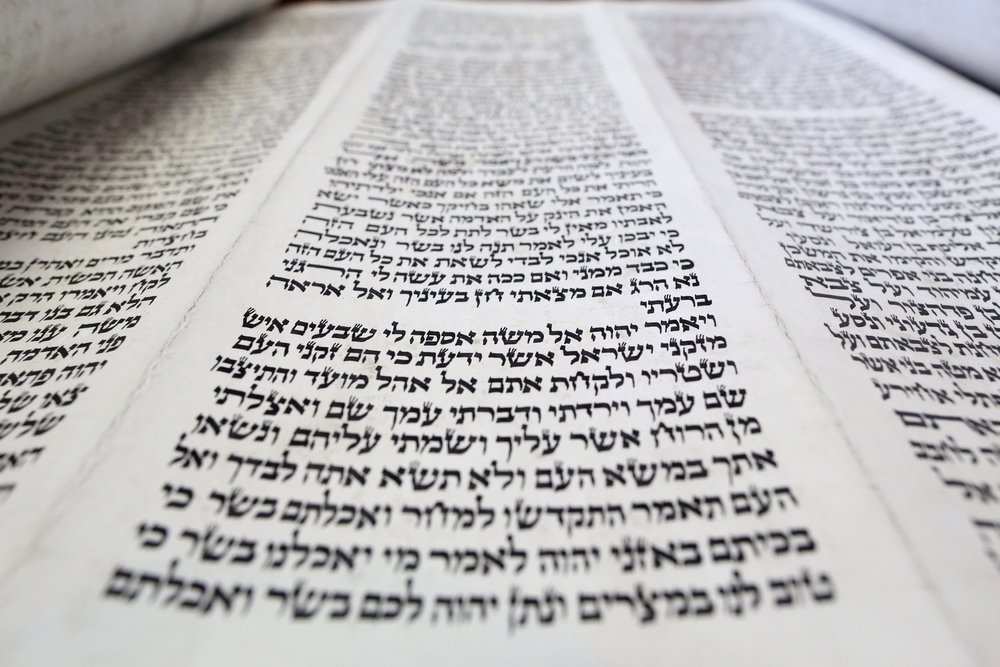 Close-up view of Hebrew scripture text written in columns on a Torah scroll - representing the concept of Biblical evidence for the existence of God.