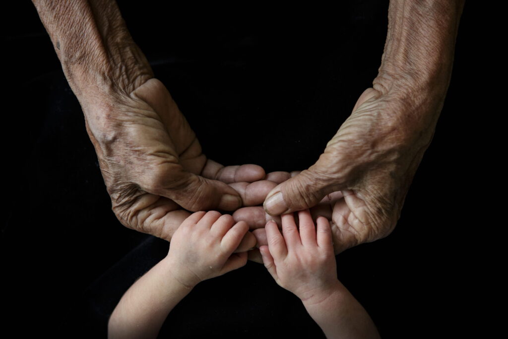 Elderly hands holding a baby’s hands, symbolizing generations and how long people lived in the Bible.
