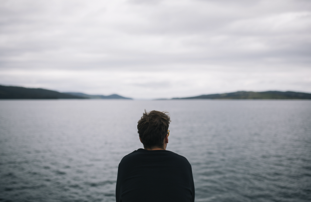 A man sitting beside the water reflecting on the God of the Bible