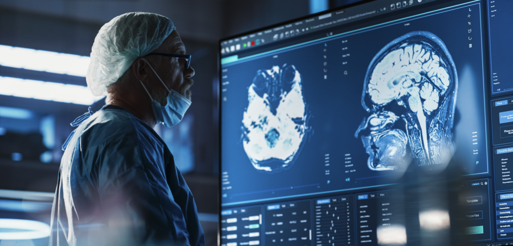 A doctor in scrubs and a face mask examines brain scans on a large screen.